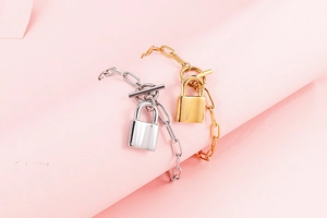 Detail of silver and gold paperclip bracelets with padlock pendants and toggle clasps