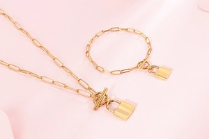 Golden titanium steel lock pendant necklace and bracelet set on soft pink background