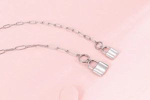 Close-up of silver steel chain with rectangular links and twin padlock pendants on pink background