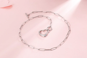 Detailed view of silver heart pendant necklace with OT clasp on a soft pink background