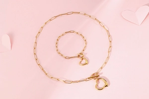 Flat lay of gold paperclip chain necklace and bracelet set with heart pendants and T-bar