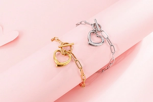 Close-up of gold and silver heart pendant bracelets with toggle clasp on pink background