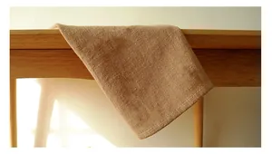 Detail of waffle-weave cotton linen napkin in camel brown draped over a wooden table