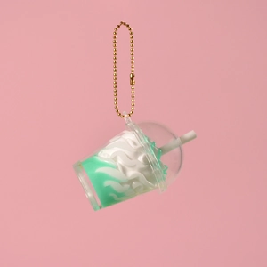 Détail d'un porte-clés miniature de tasse de thé crémeux avec chaîne dorée sur fond rose
