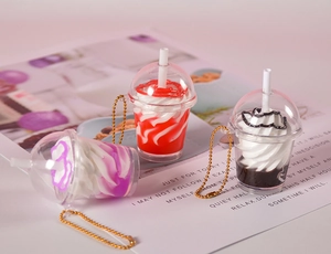Détail de mini pendentifs milkshake avec crème factice et chaînes dorées sur un magazine