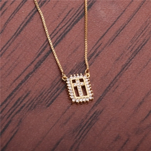 Golden box chain necklace featuring a rectangular zircon encrusted cross pendant on wood