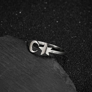 Polished silver star and moon crescent ring on grey stone background in 45-degree view