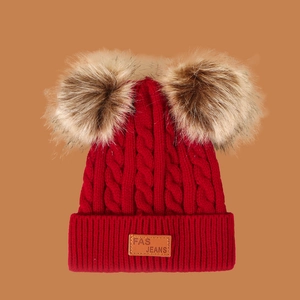 Close-up of red knit kids hat with thick cable stitch and fluffy faux fur pom-poms