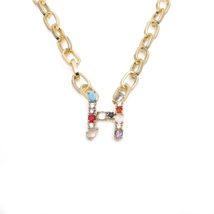 Close-up of golden necklace featuring a chunky chain and colorful rhinestone letter H pendant