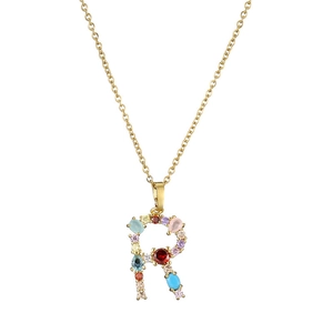 Macro detail of gold letter R pendant with multi-colored gemstone inlay and chain