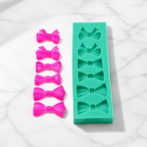 Macro view of green silicone mold with six bow shapes and pink fondant bow samples