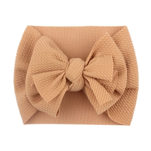 Close-up of beige baby headband with large bow in soft elastic ribbed fabric texture