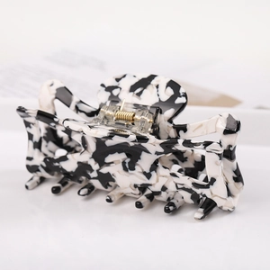 Detail of a rectangular acetate hair claw with black and white marble pattern and gold clip