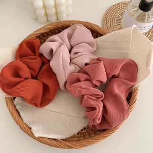 Three-piece textured fabric scrunchies set in pink and rust tones for hair styling