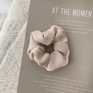 Close-up of beige fabric scrunchie with fine vertical textures on minimalist aesthetic background