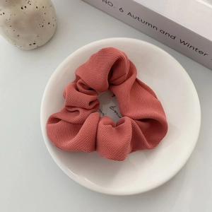 Close-up of knit texture fabric scrunchie in brick red on white ceramic plate
