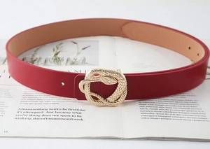 Detail of red leather belt featuring a golden snake-shaped buckle on an open book