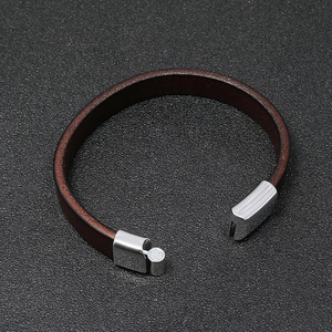 Detail view of brown leather bracelet with silver magnetic buckle on a textured surface