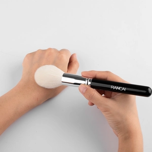Detail of soft flame-shaped highlighter brush showing fluffy bristles on hand