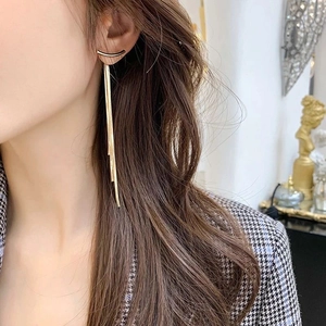 Detailed close-up of long gold fringe tassel earrings worn by a model in soft lighting