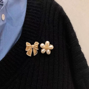 Golden bow and pearl flower brooch set displayed on a elegant black sweater