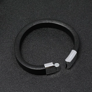 Detail of black leather bracelet featuring a silver magnetic clasp on textured background