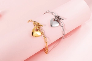 Close-up of gold and silver heart pendant bracelets with T-bar clasps on pink background