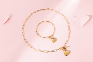 Golden paperclip chain jewelry set with heart charms and toggle closure on pink background