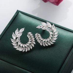 Close-up of silver zircon leaf earrings with marquise-cut stones on green satin