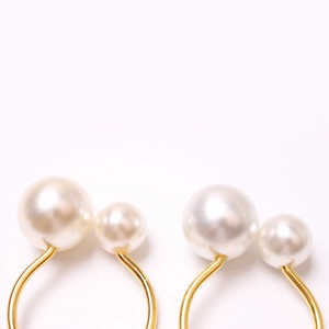 Detail of golden U-shaped napkin ring with two elegant white pearls on a white background