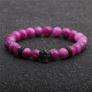 Vista macro di un bracciale con perle viola da 8mm con ciondolo a teschio nero e dettagli