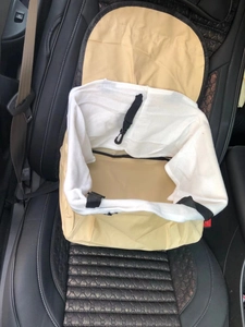 Close-up of a beige canvas pet car booster seat with nylon straps on a black vehicle seat