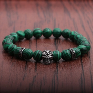 Macro shot of 8mm green malachite beads and carved silver skull on a textured surface