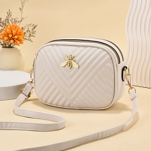 Beige quilted small square crossbody bag with gold bee logo on a decorative pedestal