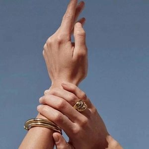 Close-up of golden croissant twist ring and bangles on hand against blue sky
