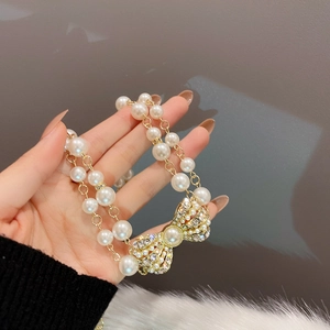 Detail of double-layer faux pearl necklace with a gold rhinestone bow pendant