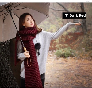 Detail of chunky knit dark red scarf with black pompom decoration for autumn winter
