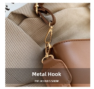 Close-up of golden metal lobster clasp and hardware detail on brown leather handbag