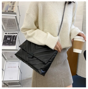 Detail of black quilted chain bag with V-shaped stitching and matte black buckle