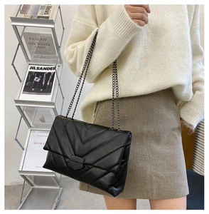 Close-up of a black quilted leather flap bag with chevron stitching and a metal chain strap
