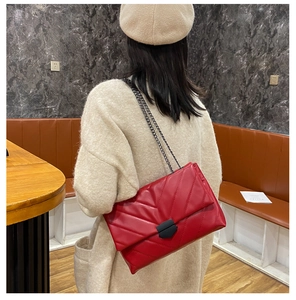 Detailed view of red quilted leather crossbody bag with V-shaped stitching and chain