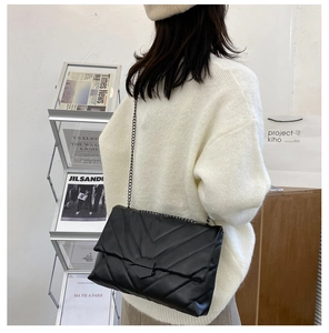 Model wearing a black V-quilted flap bag with metal chain strap in a modern lifestyle setting