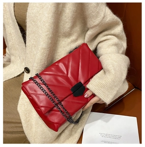 Detail of red quilted chain bag with V-shaped stitching and black metallic hardware