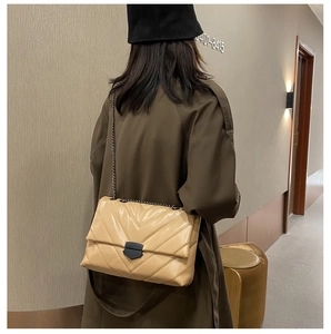 Detail of beige quilted flap crossbody bag with black metal chain and matte buckle