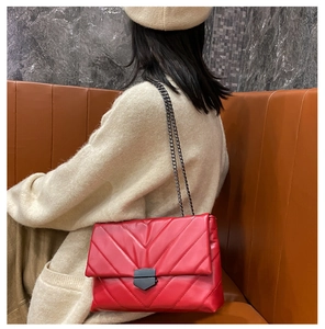 Detail of red quilted chain crossbody bag with V-pattern stitching on model