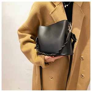 Detail of black leather bucket bag featuring a woven handle on a camel wool coat