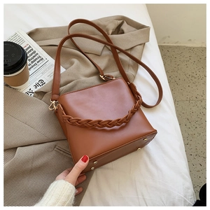 Detail of brown bucket bag with woven handle and metallic studs in office setting