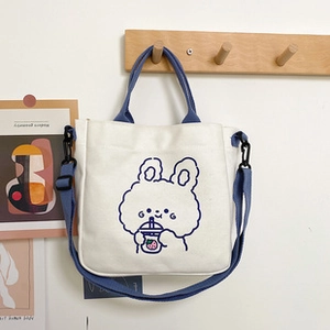 Detailed view of white canvas bucket bag with blue cartoon rabbit drinking boba tea