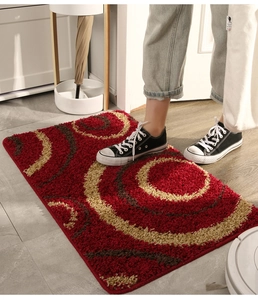 Detailed view of red plush door mat with golden circular pattern under a person's feet