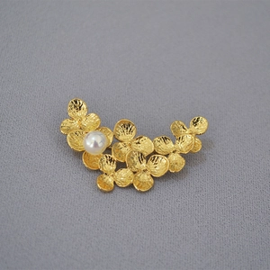 Detail of gold-plated leaf brooch showing hammered texture and elegant pearl inlay